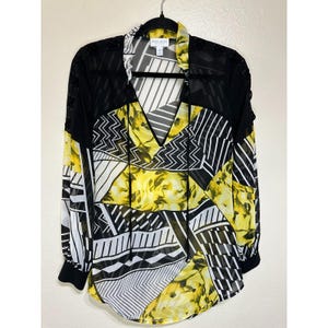 May include: Black and white geometric print blouse with yellow floral accents. The blouse has a V-neck and long sleeves.