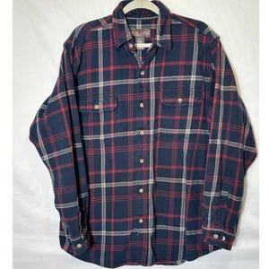 May include: A long-sleeved, button-down flannel shirt in a classic plaid pattern. The shirt features a navy blue base with red and white intersecting lines, two chest pockets, and a collared neckline. The shirt is displayed on a white hanger.
