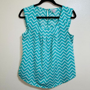 May include: A sleeveless turquoise and white chevron patterned blouse with a scoop neck and a zipper closure in the back.