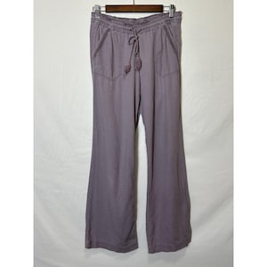 May include: Lavender-colored wide-leg pants with a drawstring waist and front pockets. The pants are hanging on a wooden hanger against a white background. The drawstring has two decorative tassels.