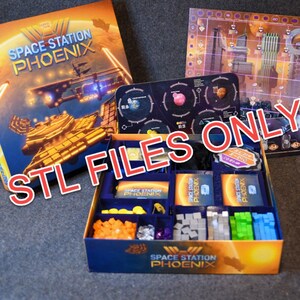 May include: A blue box with a game insert for the board game Space Station Phoenix. The insert has compartments for the game's components, including cards, dice, and tokens. The box lid is open, revealing the game's components.