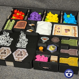 May include: A black organizer for a board game, filled with various game pieces in different colors, including red, purple, yellow, and blue. The organizer has multiple compartments for cards, tokens, and other game components. The image also shows a few game cards.