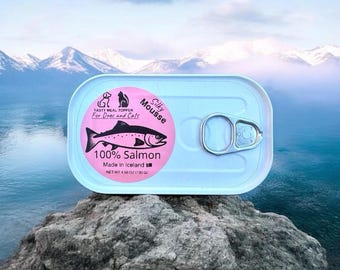 May include: A light blue rectangular can of Silky Mousse for dogs and cats, with a pink label featuring a salmon illustration. The can is labeled "100% Salmon" and "Made in Iceland". The net weight is 4.50 oz (130 g).