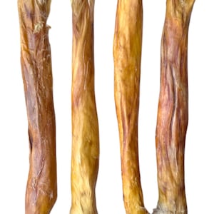 Puede incluir: Cuatro golosinas secas para perros, de color marrón claro, se muestran sobre un fondo blanco. Tienen forma cilíndrica con una superficie rugosa y texturizada. Los extremos de las golosinas tienen un material esponjoso y claro.