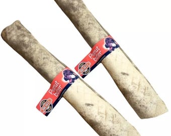 May include: Two peanut butter flavored dog chews with a brown and white color. The chews are wrapped in a red and white label with the text "Peanut Butter" and the brand name "Bravo".