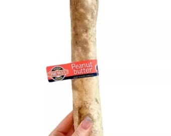 May include: A large, tan dog chew bone with a "Peanut butter" label wrapped around it. The label is red and white with the brand name "BRAVO". The bone is held by a person.