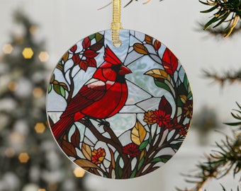 May include: A circular Christmas decoration with a stained-glass effect, depicting a red cardinal on a branch. The ornament has a gold ribbon for hanging. The bird is surrounded by colourful leaves and flowers, set against a light blue background.