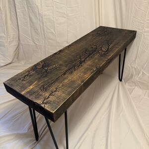 May include: A wooden bench with a dark brown stain and black lightning bolt design. The bench has black hairpin legs.