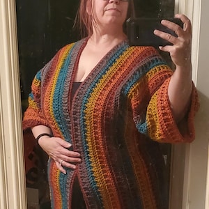 May include: A multi-colored striped crochet cardigan with a deep V-neck and long sleeves. The cardigan is made with a variety of shades of brown, orange, yellow, teal, and gray yarn.