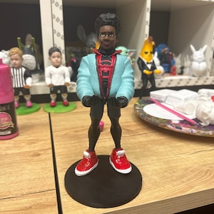 May include: A 3D printed figurine of Miles Morales, a character from the Spider-Man: Into the Spider-Verse movie. The figurine is wearing a blue and red suit with a black spider logo on the chest. The figurine is standing on a black base.