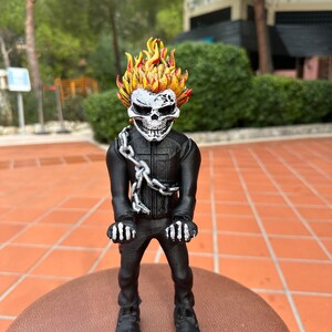 Può includere: Una statuetta stampata in 3D di Ghost Rider, un supereroe dei Marvel Comics. La statuetta è in piedi con le braccia alzate e ha una testa di teschio fiammeggiante. La statuetta è stampata in bianco e nero.