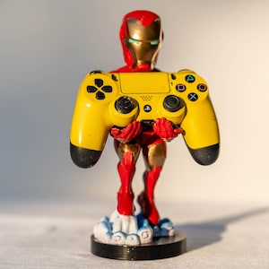 May include: A yellow and black video game controller held by a red and gold figurine of Iron Man. The figurine is standing on a cloud-shaped base.
