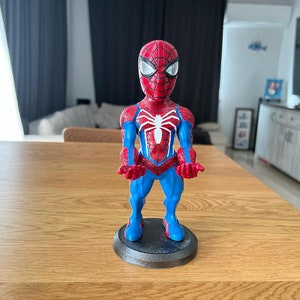 May include: A red and blue Spider-Man figurine with a white spider symbol on the chest. The figurine is standing on a black base.