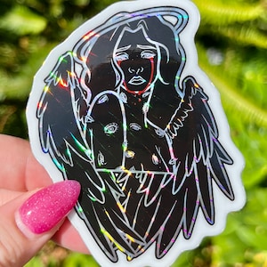 May include: A black and white sticker of an angel with wings, a halo, and eyes all over its body. The angel is crying red tears. The sticker has a holographic finish.