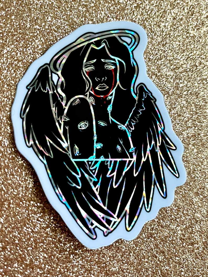 May include: A black and white sticker of an angel with wings, a halo, and eyes covering its body. The angel is crying red tears.