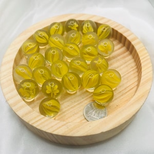 Puede incluir: Un cuenco de madera lleno de canicas de vidrio amarillo con diseños de flores blancas. Las canicas son aproximadamente del tamaño de una moneda de 20 céntimos de euro.