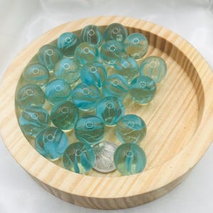 Puede incluir: Un cuenco de madera lleno de canicas de vidrio azul claro con remolinos blancos. Las canicas tienen un diámetro de aproximadamente 2,5 cm.
