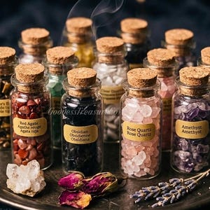 Puede incluir: Una colección de pequeños frascos de vidrio llenos de diversas piedras preciosas, incluyendo ágata roja, obsidiana y cuarzo rosa, cada uno etiquetado. Los frascos están dispuestos en una bandeja plateada, con flores y hierbas secas.