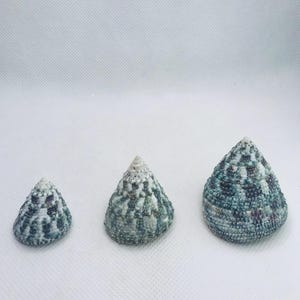 May include: A set of three ceramic mugs with a speckled, matte finish. The mugs are in shades of cream, light brown, and dark brown. Each mug has a simple, minimalist design and a rounded handle.