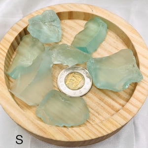 Puede incluir: Una colección de piezas de vidrio de mar azul claro sobre una superficie de madera. El vidrio de mar es de varios tamaños y formas. Se incluye una moneda canadiense como referencia de tamaño.