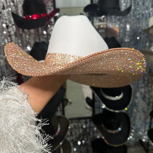 May include: A white cowboy hat with a wide brim, decorated with sparkling rhinestones in a rose gold color.