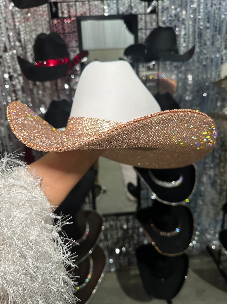 May include: A white cowboy hat with a wide brim, decorated with sparkling rhinestones in a rose gold color.