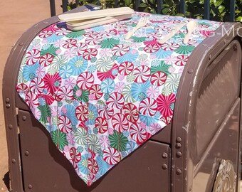 May include: A brown metal trash can with a candy cane patterned tablecloth on top. The tablecloth has red, green, white, and blue candy canes. There are two wooden utensils on the tablecloth. The trash can is in front of a body of water with a red sign that says "EPCOT" in the background.