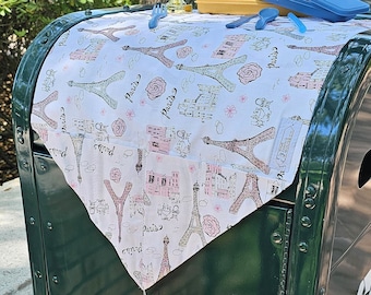 May include: A green metal trash can with a white Paris themed table runner on top. The table runner has a tassel and features a repeating pattern of the Eiffel Tower, hearts, and the word "Paris".