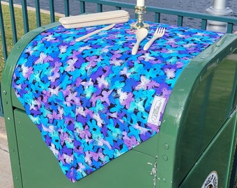 May include: A green metal trash can with a blue and purple butterfly patterned fabric placed on top. The fabric has a white border and the words "Help Keep Our Parks Clean" are printed on the fabric. The trash can has a sign that says "Please Help Keep Our Parks Clean".
