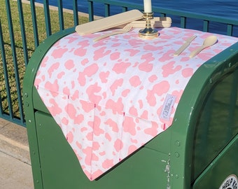 May include: A green metal trash can with a pink and white cow print liner. The liner has a white candle holder with a white candle in it. There are also two plastic utensils on the liner.