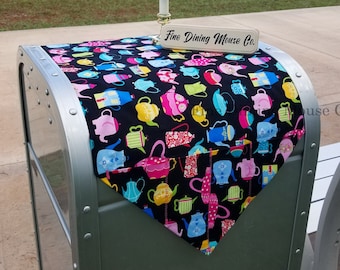 May include: A black table runner with a colorful teacup pattern. The runner is on a metal table with a sign that reads "Fine Dining Mouse Co."