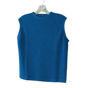 May include: A sleeveless, teal-colored top hangs on a clear plastic hanger. The top has a crew neck and a textured knit fabric. The garment is a solid color and appears to be made of a soft material.