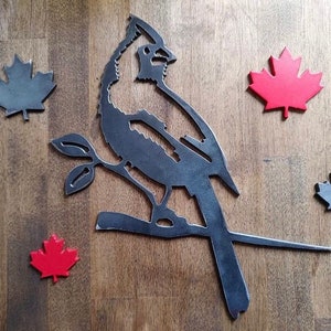 May include: Metal wall art featuring a cardinal perched on a branch with three red maple leaves and two gray maple leaves on a wood background.
