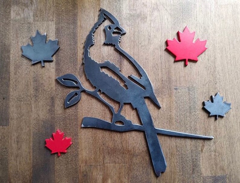 May include: Metal wall art featuring a cardinal perched on a branch with three red maple leaves and two gray maple leaves on a wood background.