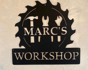May include: Black metal sign with a saw blade design and the text "Marc's Workshop". The saw blade has three tools inside: a hammer, a wrench, and a screwdriver.