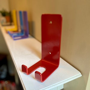 May include: A red metal wall mount with two hooks. The mount is attached to a white shelf.