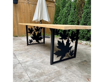 May include: A wooden outdoor dining table with black metal legs featuring a maple leaf design.