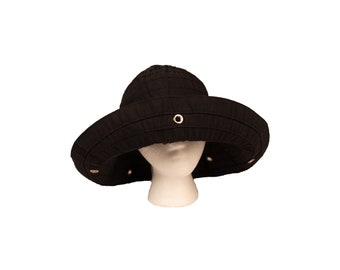 May include: A black wide-brimmed hat featuring a rounded crown and horizontal stitching along the brim. The hat is accented with evenly spaced metallic gold-toned grommets embedded into the fabric of the brim, providing a structured appearance.