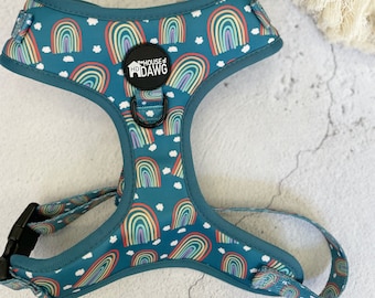 May include: Teal dog harness featuring a repeating rainbow pattern with white clouds. The harness has a black buckle and a metal D-ring. The brand logo "HOUSE of HDDAWG" is visible on the harness. A rainbow-shaped dog toy is in the background.