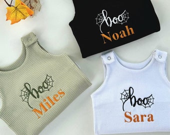May include: Three baby Halloween outfits in black, light green, and white. Each outfit has a ribbed texture and features the word "boo" with a spiderweb design, along with a personalized name in orange. The outfits are sleeveless with snap closures.