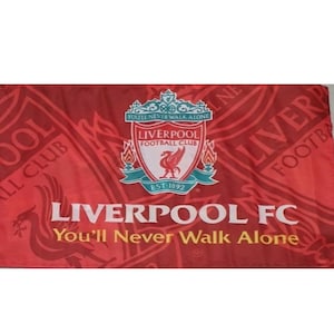 Peut inclure: Un drapeau rouge du Liverpool FC avec l'emblème de l'équipe et les mots "You'll Never Walk Alone".