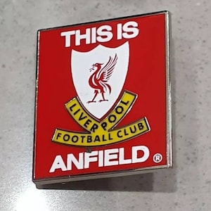 Könnte beinhalten: Eine rote und weiße Emaille-Anstecknadel mit dem Wappen des Liverpool Football Club und den Worten "This is Anfield".
