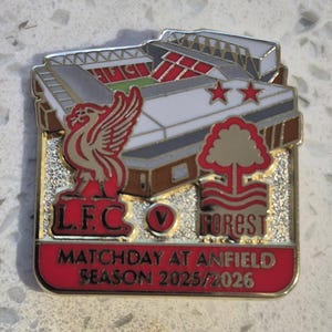 Puede incluir: Pin rectangular con borde dorado, que presenta un estadio, logotipos de equipos y texto. La base del pin es roja, con el texto "MATCHDAY AT ANFIELD SEASON 2025/2026". El estadio es gris y blanco con asientos rojos.