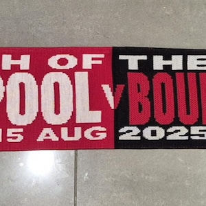 Può includere: Una sciarpa da calcio rossa e nera con la scritta "MATCH OF THE DAY LIVERPOOL 15 AUG 2025" e "BOURNEMOUTH". Presenta loghi delle squadre e la parola "CHAMPIONS" sulla sezione rossa.
