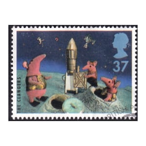 Puede incluir: Un sello postal británico que representa una escena de "The Clangers". El sello muestra criaturas rosas parecidas a osos hormigueros en una superficie lunar con un cohete y un cielo estrellado. El sello tiene una silueta azul de una persona y el número 37.
