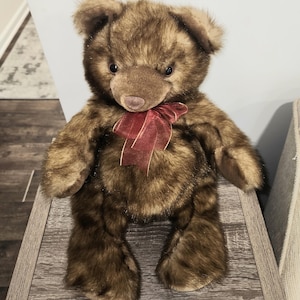 May include: A brown plush teddy bear with a red bow sitting on a wooden surface.