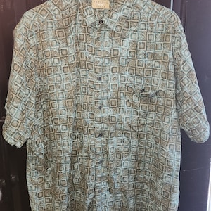 May include: A short-sleeved button-down shirt with a geometric pattern in shades of blue and brown. The shirt has a label that reads "Natural  Trance".