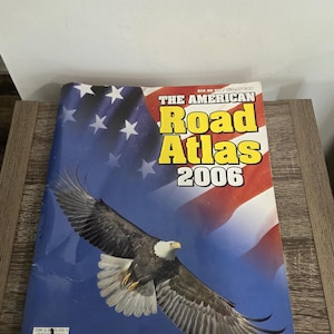 Puede incluir: Atlas de carreteras americano de 2006, con un águila calva sobre un fondo de la bandera estadounidense. La portada incluye el texto "United States/Canada/Mexico" y el logotipo del editor.