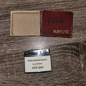 May include: A silver lighter with a white label that reads "Thunderbird Lanes 225 Club". The lighter is in its original box, which is red with gold lettering that reads "Rubylite".