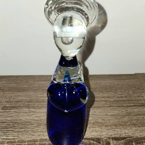 May include: A cobalt blue glass sculpture of a stylized bird with a clear glass head and a clear glass top.